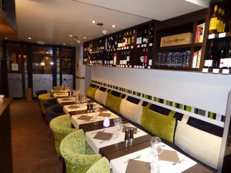 Tables dressées dans un restaurant à Aurillac, idéal pour un repas du dimanche. Les étagères débordent de bouteilles de vin.
