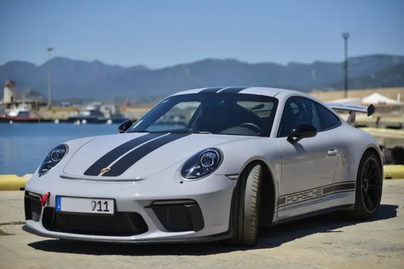 Szary Porsche 911 z czarnymi pasami, stojący nad wodą. Zastanawiasz się nad porsche 911 cena?