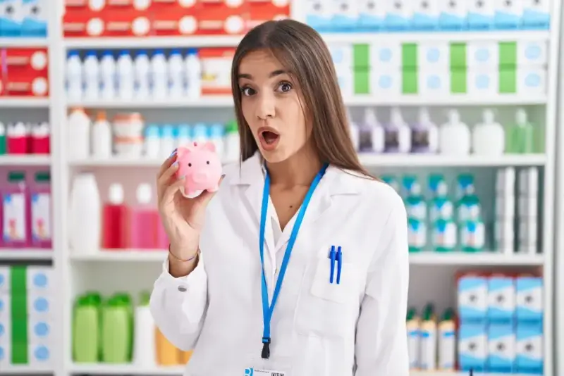 Zaskoczona farmaceutka trzyma skarbonkę, zastanawiając się, ile zarabia technik farmacji.