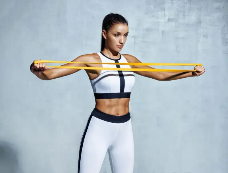 Femme athlétique travaillant ses pectoraux avec un élastique jaune.