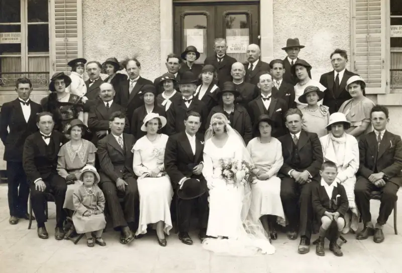 Un groupe pose pour une photo de mariage, peut-être pour un registre mariage. La mariée porte une robe blanche et un voile.