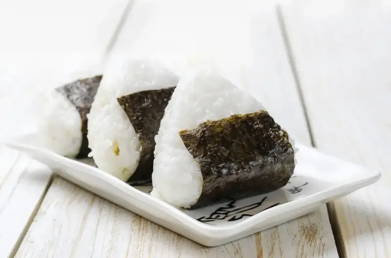 Trzy ryżowe kulki onigiri z nori na białym talerzyku. Idealne na szybki lunch, gdy szukasz prostego onigiri przepis.