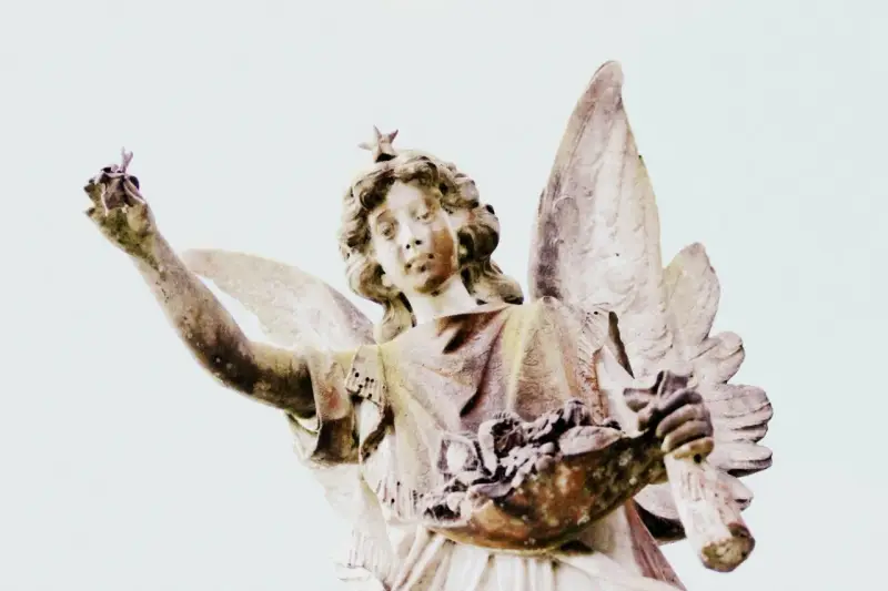 Kamienna figura anioła z gwiazdą na głowie, trzymająca w dłoniach kwiaty i gałązkę. Symbolika 2244 znaczenie.