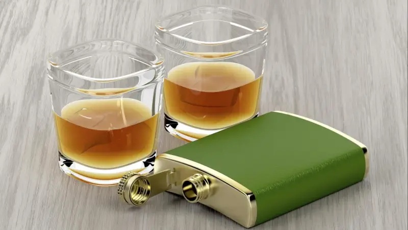 Zwei Gläser mit bernsteinfarbenem Whiskey und ein grüner Taschenflachmann. Ein 4 cl Whiskey hat ca. 90 Kalorien.