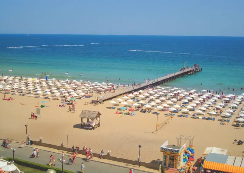 Słoneczny Brzeg, Bułgaria: tłumy plażowiczów, białe parasole, molo i turkusowe morze.