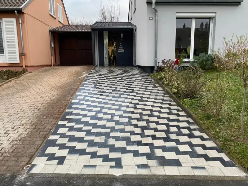 Une allée en pavé au motif géométrique noir et blanc mène à une entrée de garage.