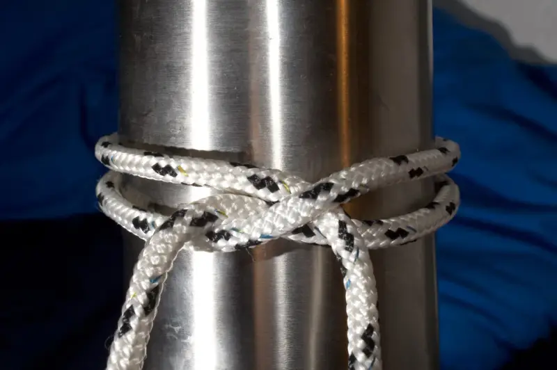 Un nœud pare battage, simple et efficace, sécurise une corde blanche et noire autour d'un mât métallique.