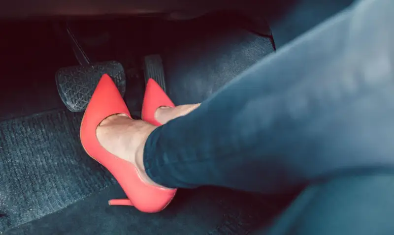 Piedi con tacchi rossi sui pedali dell'auto. Dimostra che si può guidare con i tacchi, con stile e sicurezza.