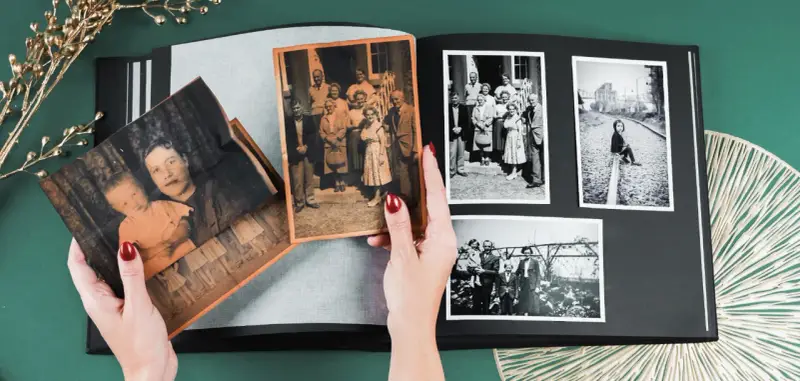 Ręce układają stare fotografie w albumie, pokazując, jak skanować zdjęcia i zachować wspomnienia.