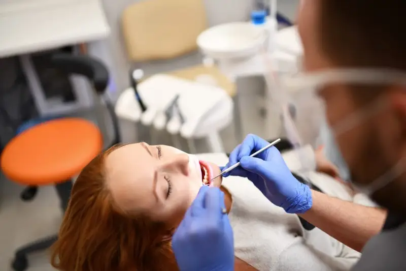 Pacjentka z rudymi włosami u dentysty. Badanie jamy ustnej, które może być związane z diagnostyką twardziny układowej.