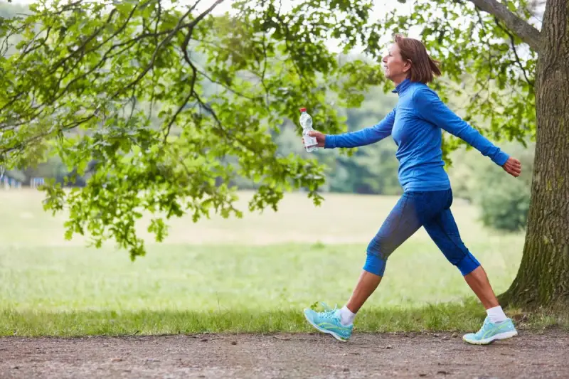 Femme souriante en tenue de sport bleue, profitant de 30 minutes de marche rapide par jour dans un parc verdoyant.