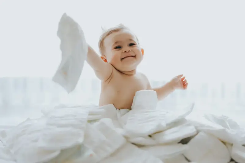 Uśmiechnięty bobas otoczony stertą pieluch. Zastanawiasz się, jakie pieluchy dla noworodka będą najlepsze?