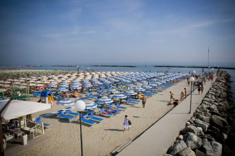 Spiaggia affollata a Gatteo Mare centro, con file di ombrelloni e lettini, gente che passeggia sul molo e si gode il sole.