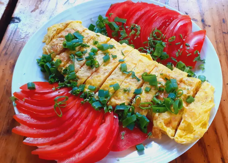 Pyszne koreańskie śniadanie: pokrojony omlet z jajek posypany szczypiorkiem, podany z plasterkami pomidora.