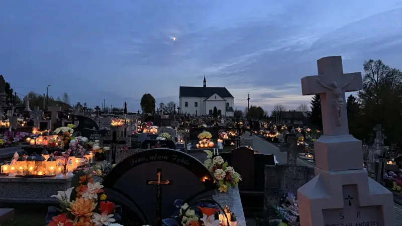 Cmentarz nocą, pełen płonących zniczy i kwiatów. W oddali kościół, a na niebie księżyc. Modlitwa świętej Gertrudy w ciszy zadumy.