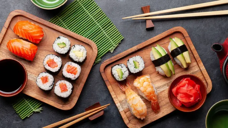 Frischer roher Fisch stillt den Appetit auf Sushi. Nigiri mit Lachs, Maki-Rollen mit Avocado und Garnelen-Sushi auf Holzbrettern.