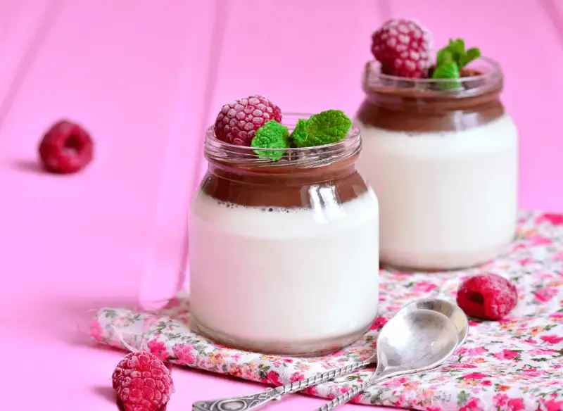Två glas med choklad- och vaniljpannacotta, toppade med hallon och mynta. Perfekt som dessertvin till pannacotta.