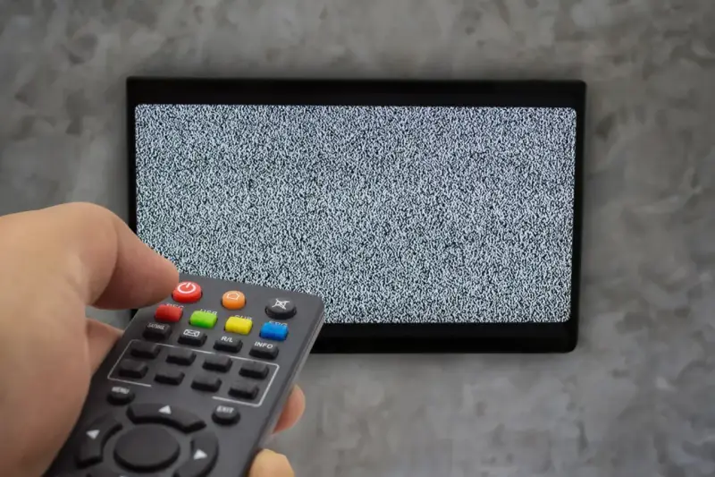 Ręka trzyma pilot dekodera, celując w ekran telewizora z zakłóceniami. Czas na naukę, jak sparować pilot dekodera z telewizorem.