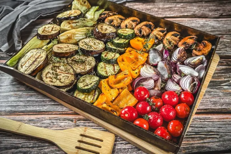 Buntes Gemüse wie Auberginen, Zucchini, Paprika, Zwiebeln und Tomaten auf einem Blech für ein köstliches vegetarisches Grillen.