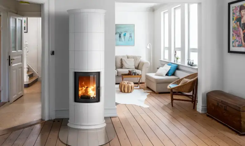 Un élégant poêle de masse blanc diffuse une douce chaleur dans un salon lumineux aux planchers de bois.