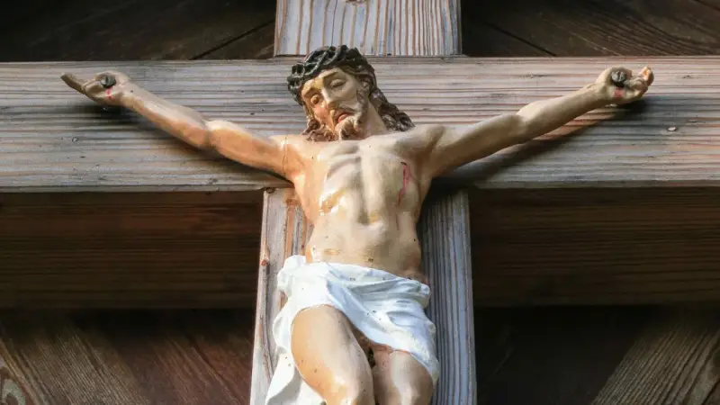 Jesus gekreuzigt, mit Dornenkrone und Wunden, hängt an einem Holzkreuz.