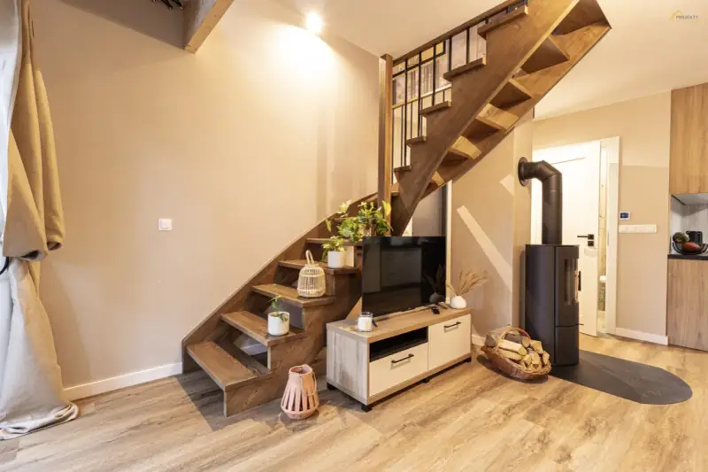 Przytulny dom z bali 70m2 cena. Drewniane schody, kominek, TV i stylowe dodatki tworzą ciepłą atmosferę.
