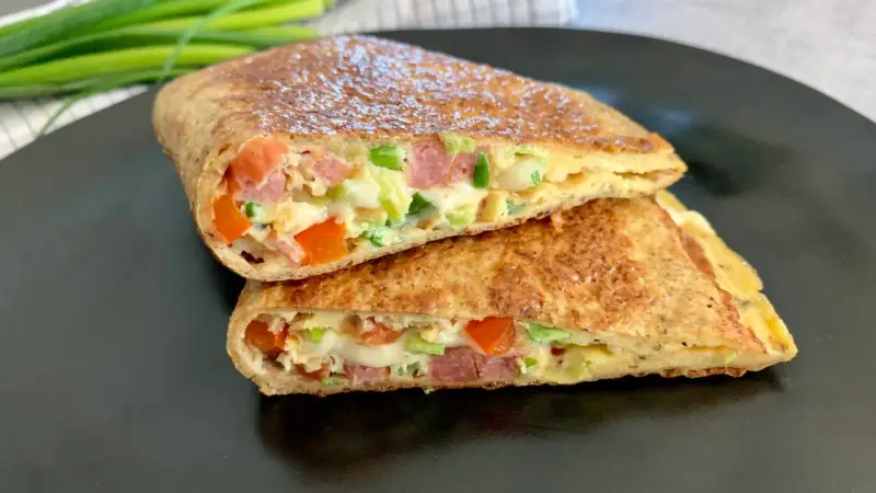 Keto tortilla z jajkiem, warzywami i wędliną, pokrojona na pół, prezentuje apetyczny przekrój.