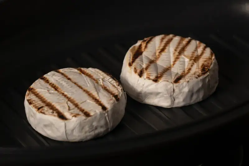 Due forme di formaggio da fare alla piastra, con belle striature dorate, cuociono in una padella scura.