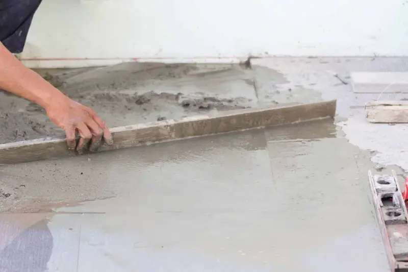 Ręka wyrównuje świeży beton, tworząc idealnie gładką podłogę na gruncie.