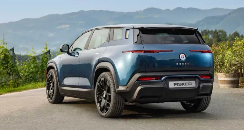 Tylna część niebieskiego elektrycznego SUV-a Fisker Ocean na tle gór i zieleni.
