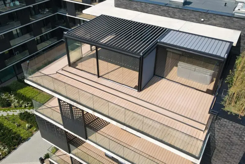 Nowoczesny taras na dachu z przeszklonym pawilonem i pergolą. Drewniana podłoga i szklane balustrady tworzą elegancką przestrzeń.