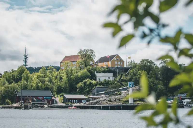 Widok na wybrzeże w Kristiansand, Norwegia. Żółte budynki na wzgórzu, czerwony klub kajakowy i wieża telekomunikacyjna.