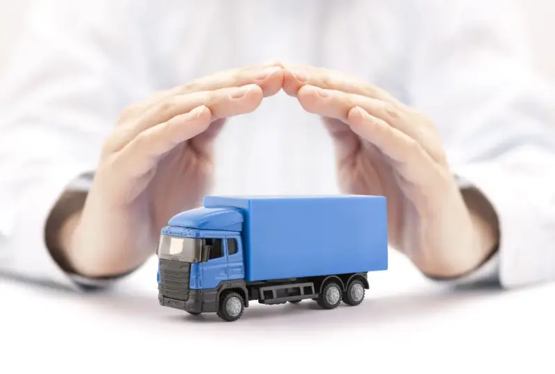 Ręce chronią niebieską ciężarówkę, symbolizując ubezpieczenie AC w kosztach transportu.