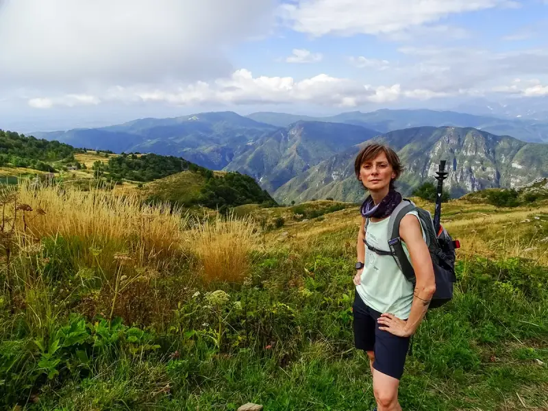 Donna con zaino e bastoncini da trekking ammira il panorama montuoso, un'emozione delle camminate FVG.