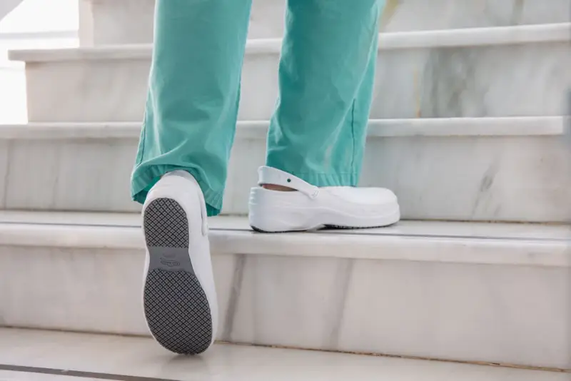 Persona subiendo escaleras con zapatos blancos, mostrando la suela antideslizante. El poliuretano en zapatos ofrece comodidad y durabilidad.