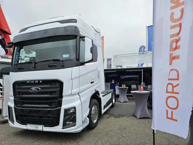 Biały Ford F-MAX prezentuje się na wystawie, obok banerów z logo Ford Trucks.
