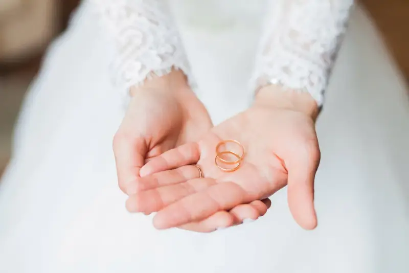 Zwei goldene Eheringe liegen in den Händen einer Braut. Sie sind ein Symbol für ihre bevorstehenden Hochzeitstage und die Namen, die sie für immer verbinden werden.