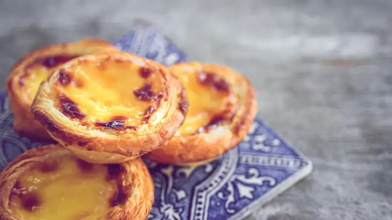 Ein Stapel goldbrauner, karamellisierter Pastel de Nata auf einer blauen Kachel.