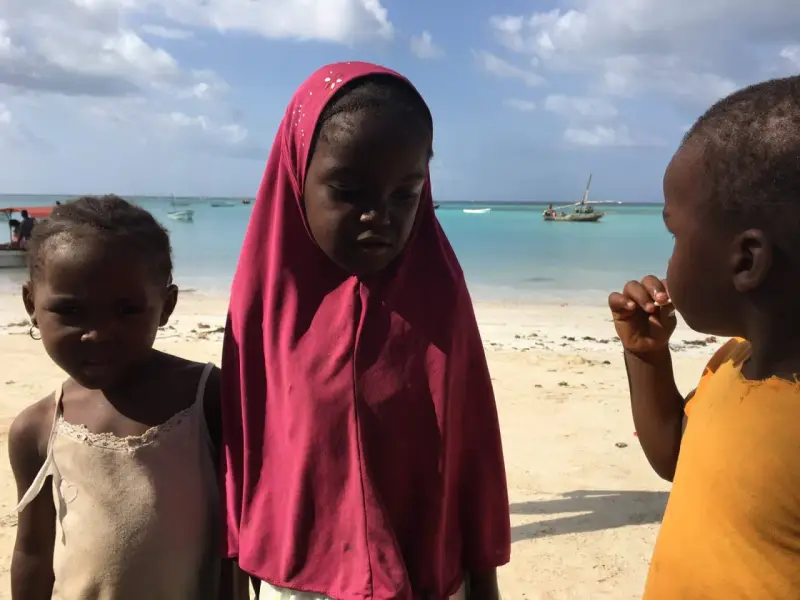 Dzieci na plaży, w tle turkusowe morze i łodzie. To obrazek z życia na Zanzibarze.