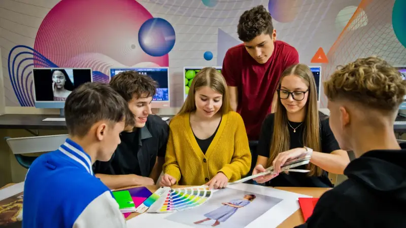Grupa młodych ludzi dyskutuje nad próbkami kolorów i zdjęciami przy biurku.