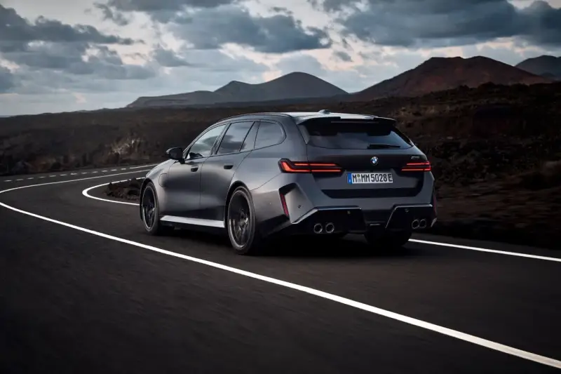 Mocne BMW M5 Touring pędzi po krętej drodze pośród surowego krajobrazu.