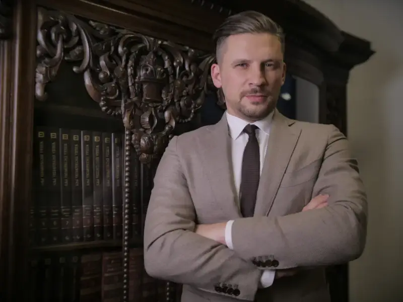 Mężczyzna w garniturze stoi na tle regału z książkami.