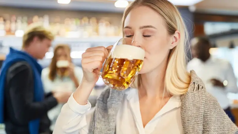 Kobieta z zamkniętymi oczami pije piwo bezalkoholowe w ciąży, ciesząc się smakiem w pubie.