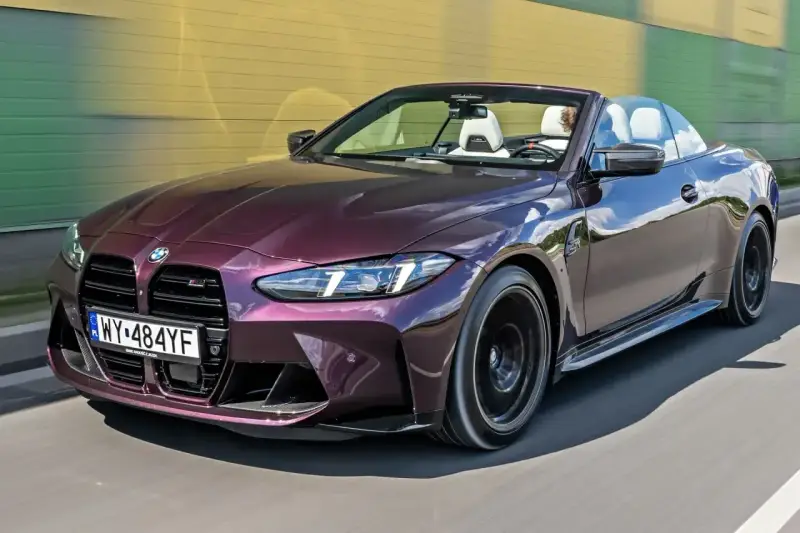 Fioletowe BMW M4 Competition kabriolet pędzi po drodze, odsłaniając białe wnętrze i sportowe detale.