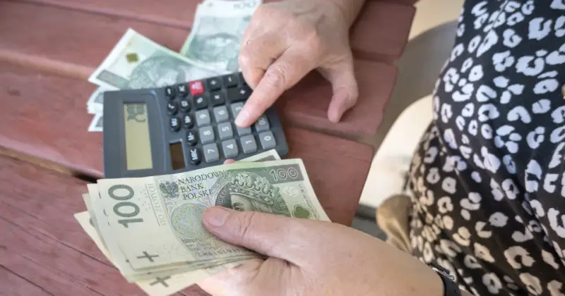 Ręce liczą banknoty 100 zł przy kalkulatorze. Może to być pomocne przy analizie nowych zasad przejścia na emeryturę tabela.