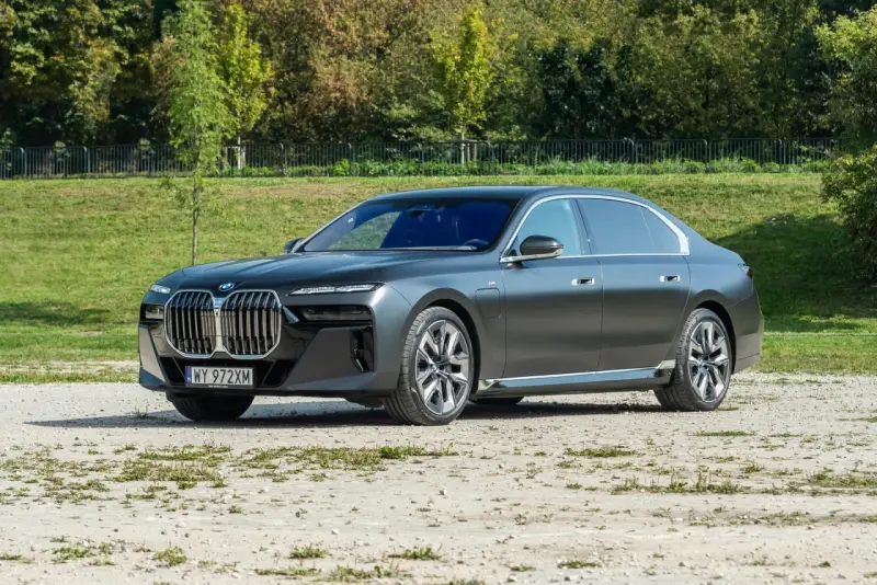 Elegancki, grafitowy BMW 740d na tle zieleni. Luksusowa limuzyna prezentuje się imponująco.