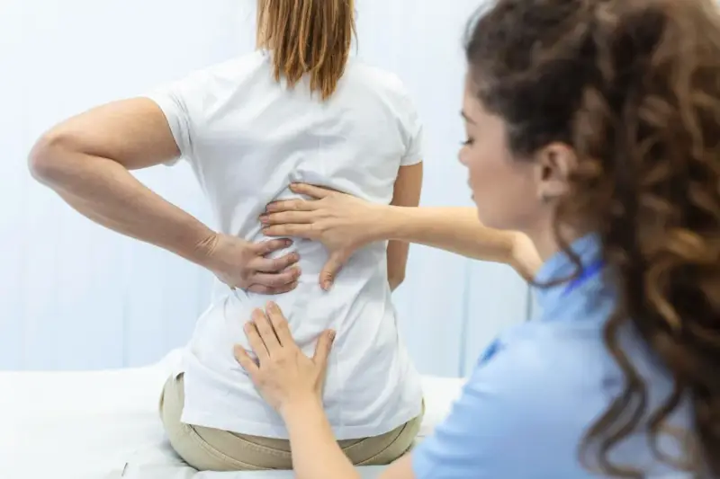 Fizjoterapeuta bada plecy pacjentki. Po długiej rehabilitacji wreszcie wyleczyłem kręgozmyk i czuję się znacznie lepiej.