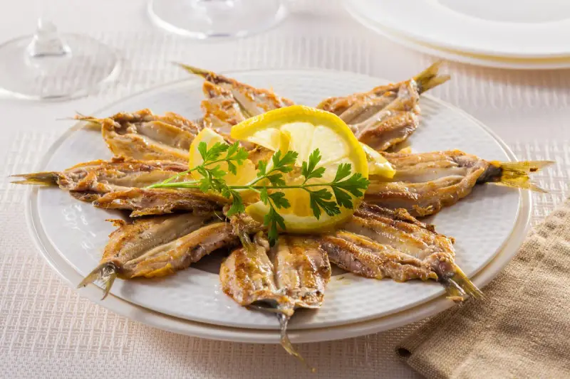 Piatto di alici alla scapece disposte a raggiera, guarnite con fette di limone e prezzemolo.
