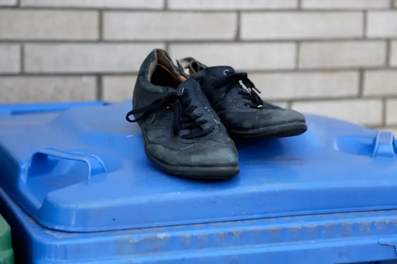 Stare, czarne buty leżą na niebieskim koszu na śmieci. Czas zastanowić się, gdzie wyrzucić stare buty, by dać im drugie życie.