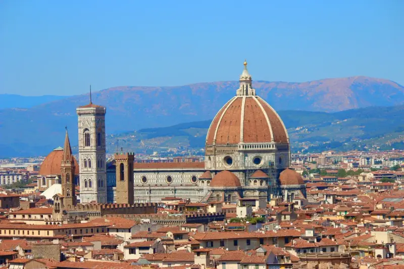 Vue panoramique de Florence avec le **dôme de Brunelleschi** dominant la ville, sous un ciel bleu clair.